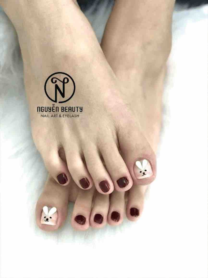 Bộ nail chân được sơn màu đỏ rượu, với ngón cái trang trí họa tiết hình chú thỏ trắng